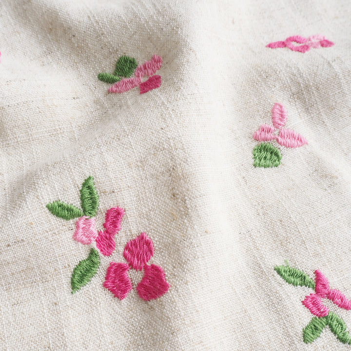 Close-up of embroidered pink flowers and green leaves on beige fabric.