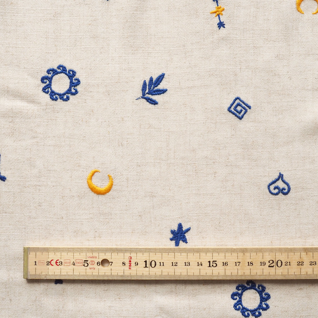 Textile with embroidered patterns and a ruler for scale on a beige background