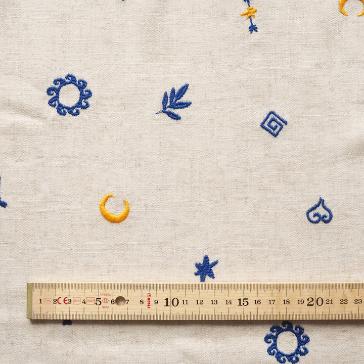 Textile with embroidered patterns and a ruler for scale on a beige background