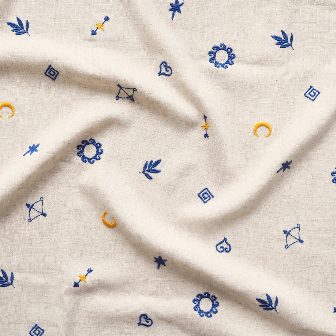 Textured fabric with embroidered patterns including stars, moons, and arrows on a beige background.