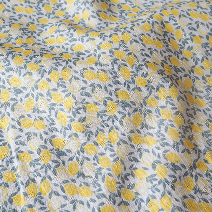 Fabric with a pattern of yellow lemons and green leaves on a pale background
