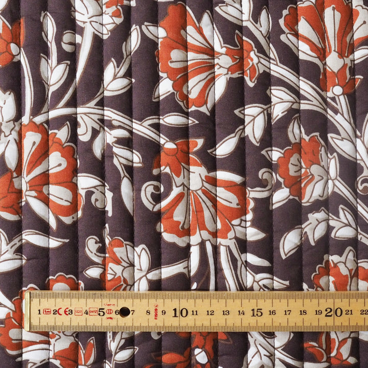 Floral fabric with orange and white flowers on a brown background, measured with a ruler.