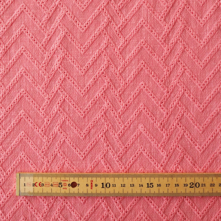 Pink fabric with a zigzag pattern and a wooden ruler at the bottom for scale.