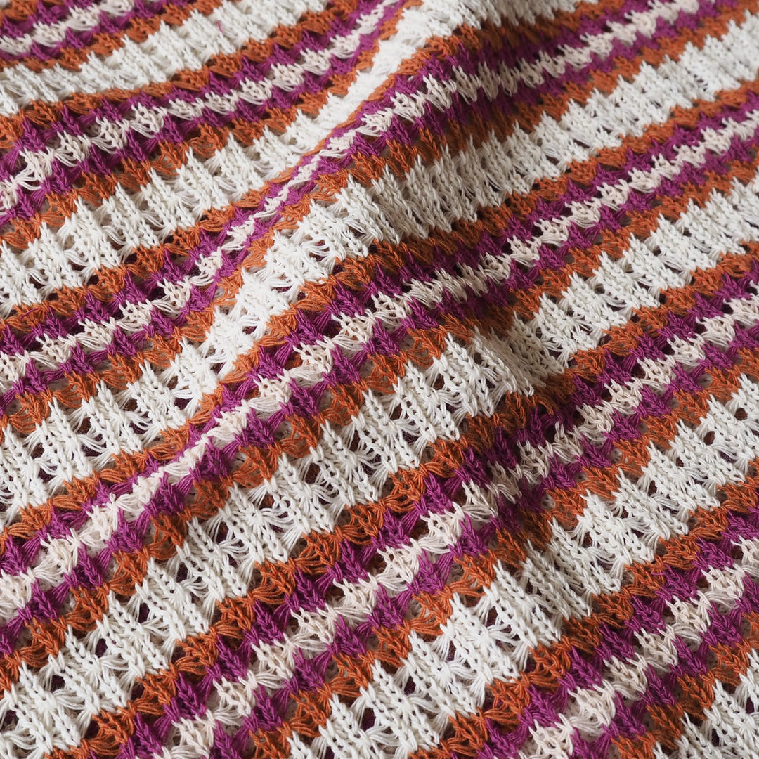 Close-up of a knitted fabric with pink, orange, and white stripes.