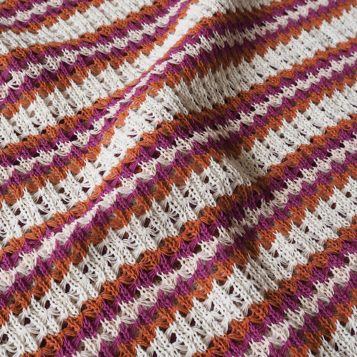 Close-up of a knitted fabric with pink, orange, and white stripes.
