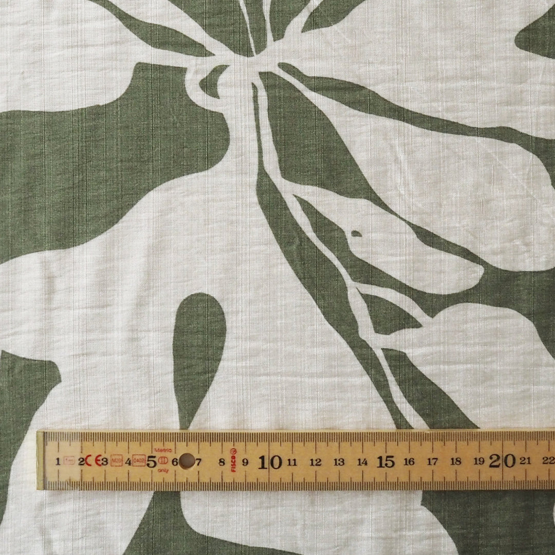 Fabric with green leaf pattern and a ruler for scale on a beige background