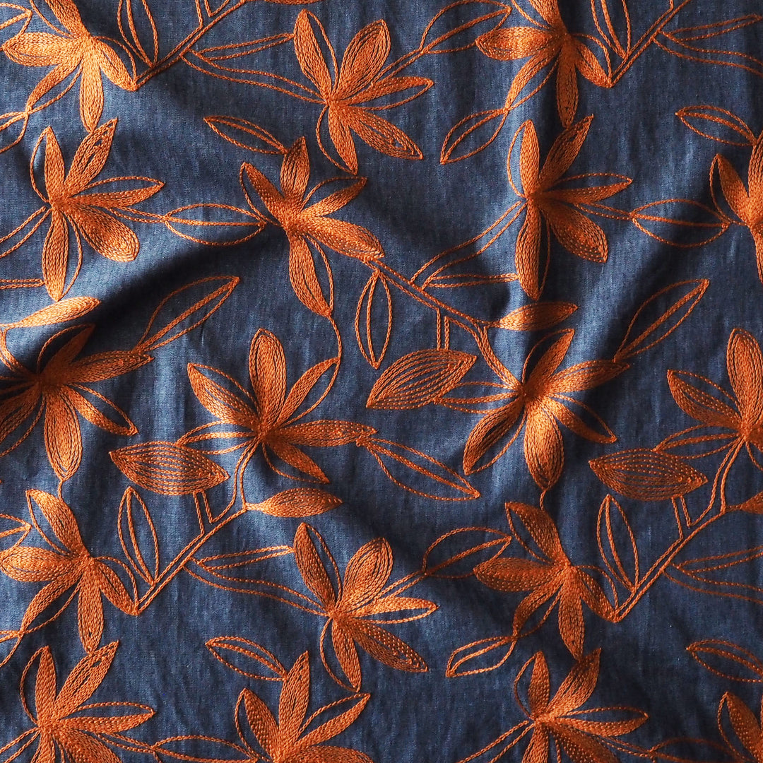A close-up of a dark blue fabric with an embroidered orange floral pattern.