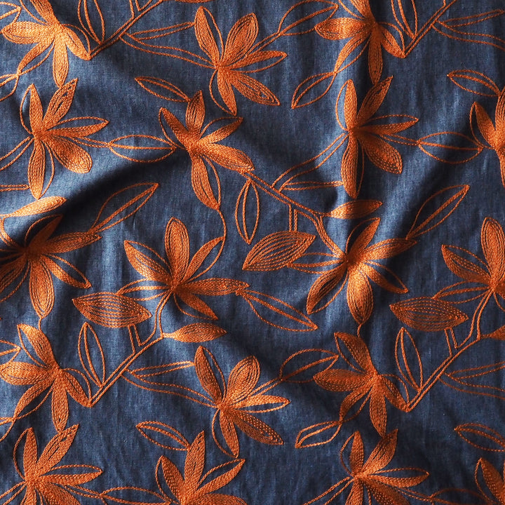 A close-up of a dark blue fabric with an embroidered orange floral pattern.