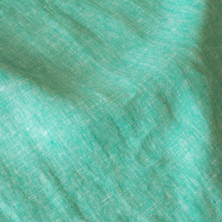 A close-up of textured fabric in a bright mint green or aqua tone, filling the frame with visible weave and soft folds.