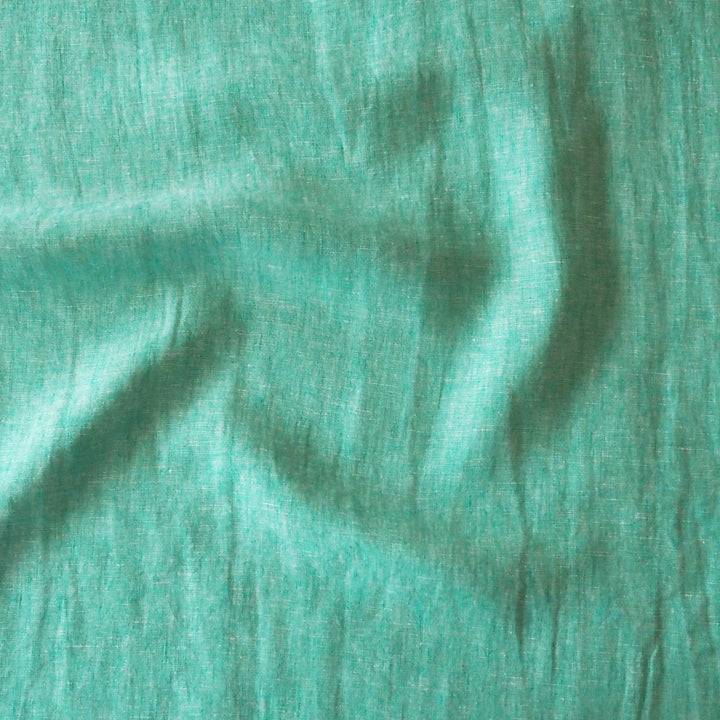 A close-up of a textured fabric in a muted teal-green color, showing soft folds and a slightly crinkled weave.