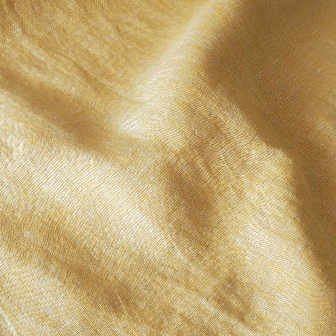 A close-up of draped light yellow fabric with a soft woven texture and gentle shadows.