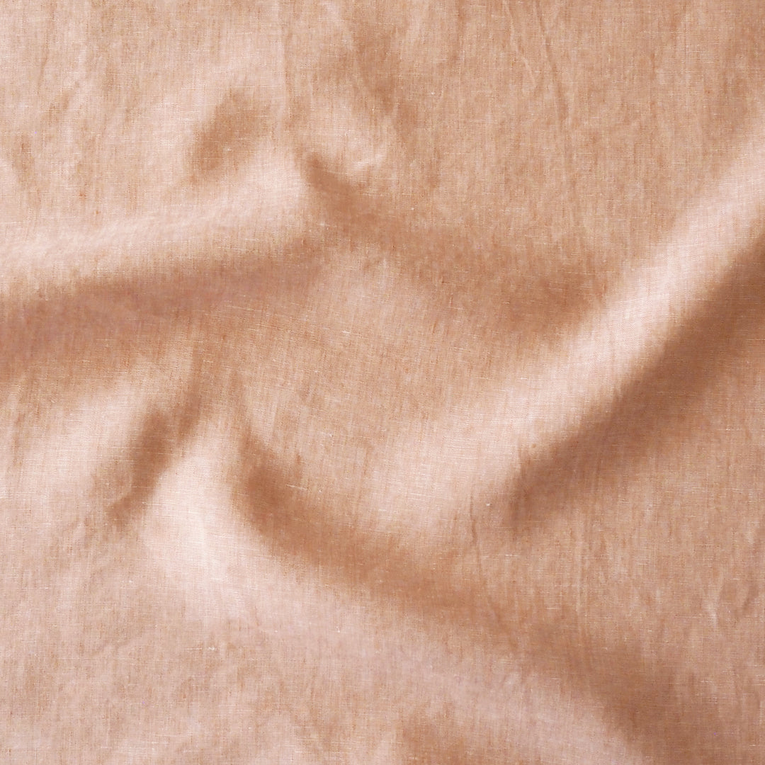 A close-up of draped peach-beige fabric with a soft, slightly sheer texture and gentle folds.