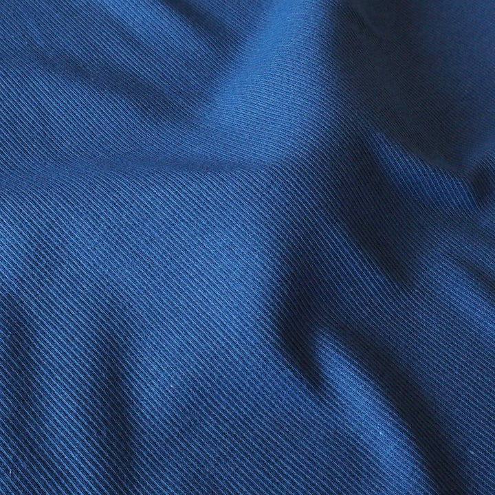 A close-up of textured blue fabric with a diagonal twill weave and soft folds.