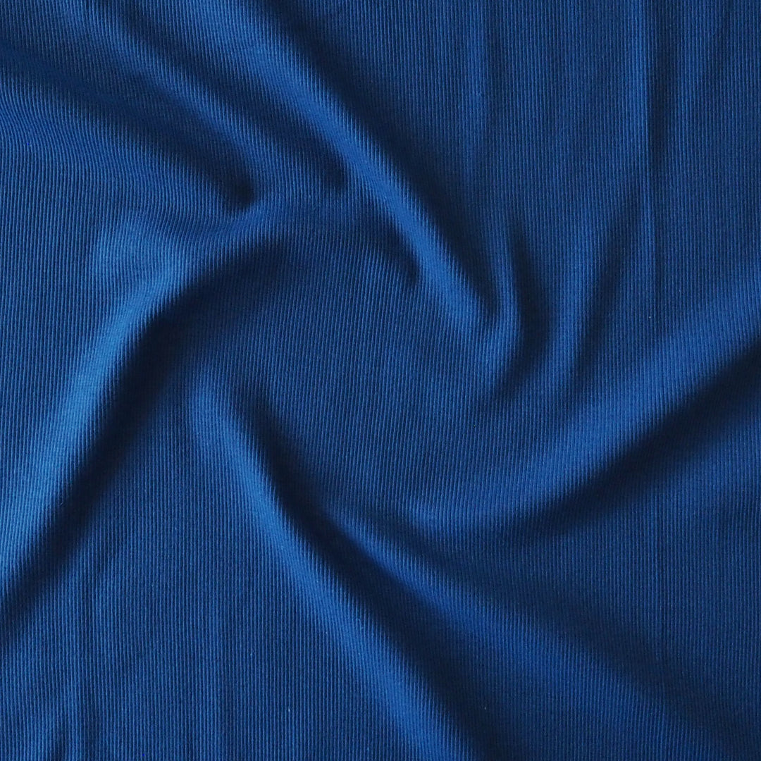 A close-up of royal blue ribbed fabric with soft swirls and folds, filling the entire frame.