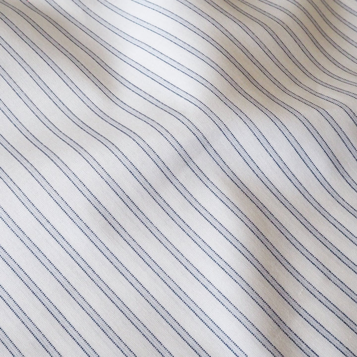 A close-up of white fabric with thin, evenly spaced navy blue pinstripes running diagonally across the surface.