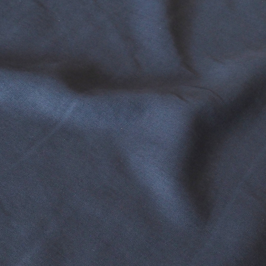 A close-up of dark navy blue fabric with soft folds and a smooth texture.