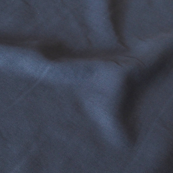 A close-up of dark navy blue fabric with soft folds and a smooth texture.
