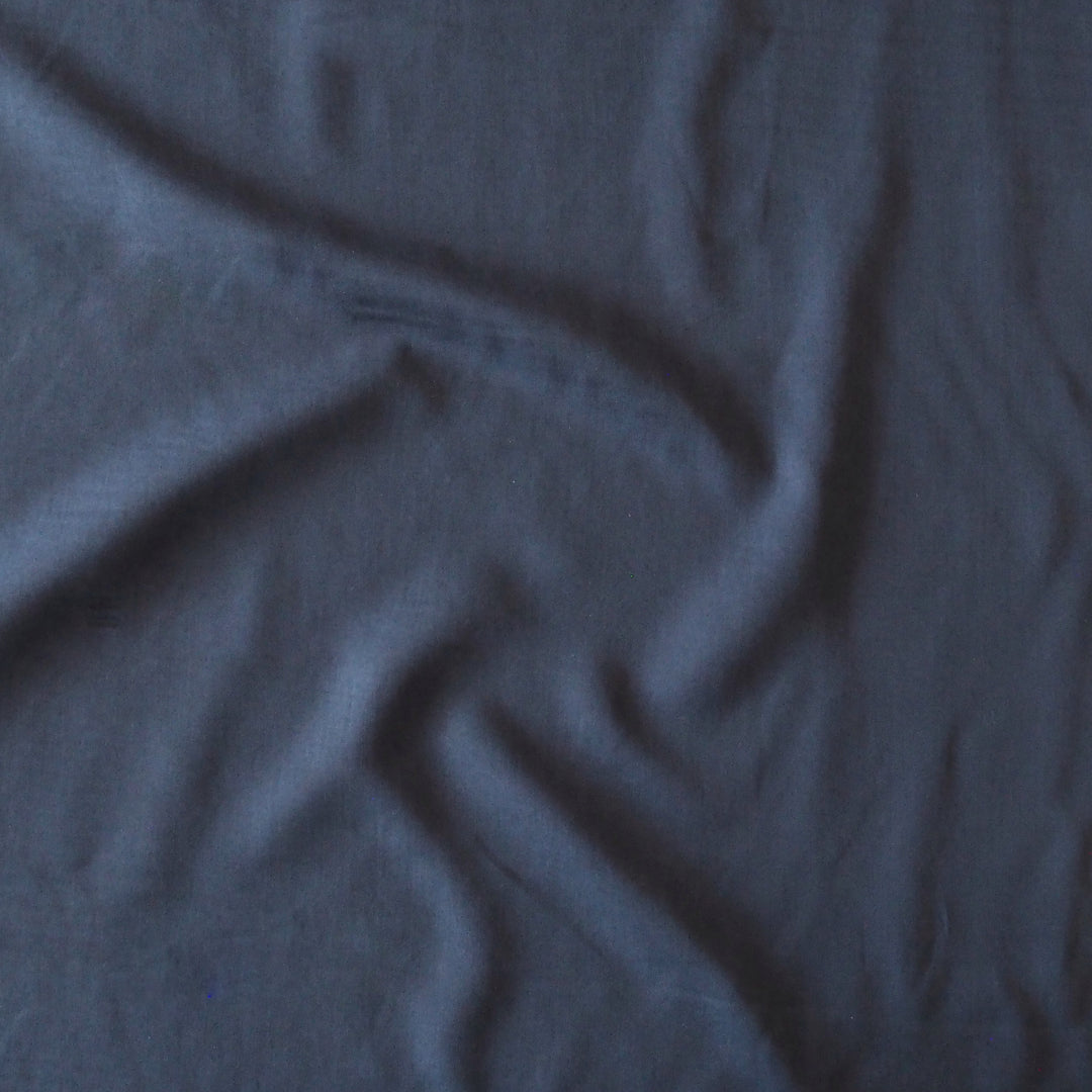 A close-up of draped dark slate blue fabric with soft folds and a matte texture.