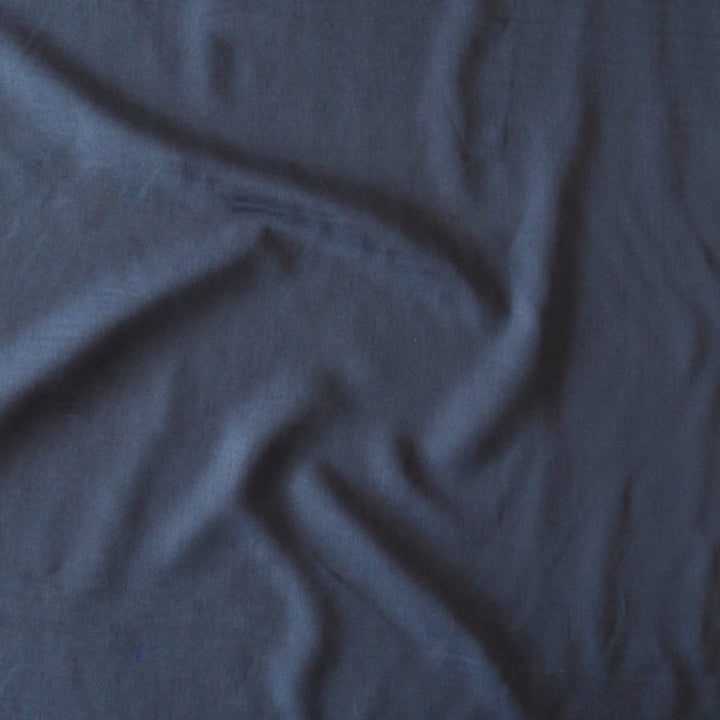 A close-up of draped dark slate blue fabric with soft folds and a matte texture.