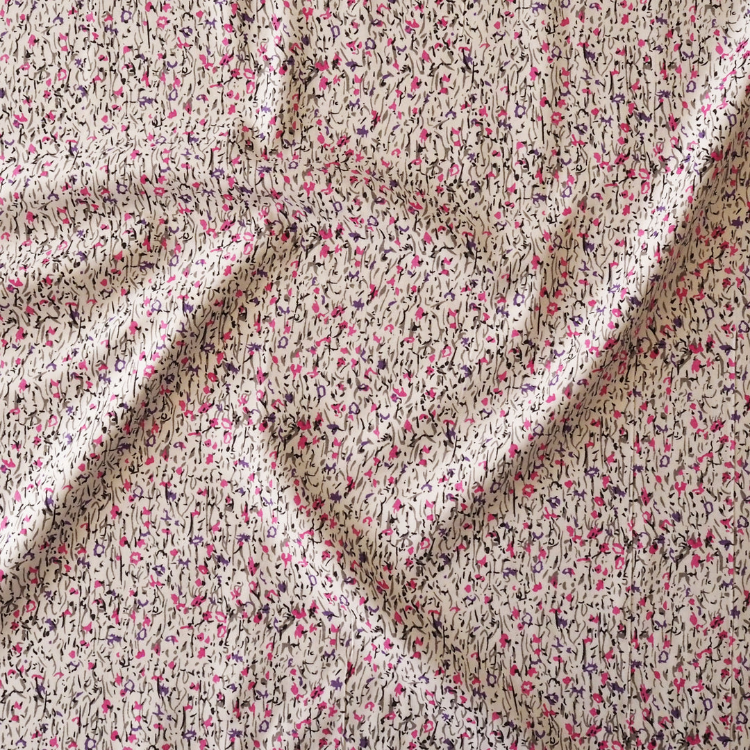 A close-up of draped fabric with a dense abstract print featuring pink, black, and dark gray brushstrokes over a warm beige background.