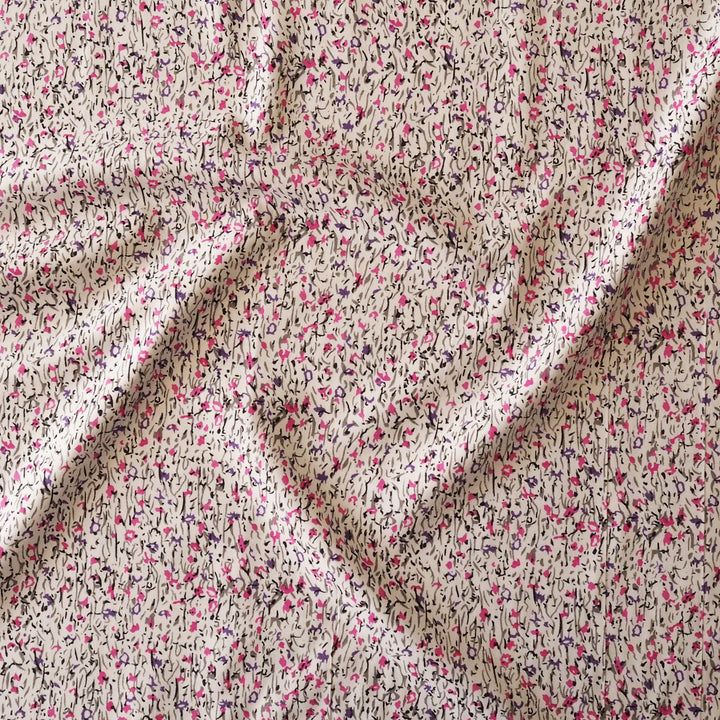 A close-up of draped fabric with a dense abstract print featuring pink, black, and dark gray brushstrokes over a warm beige background.