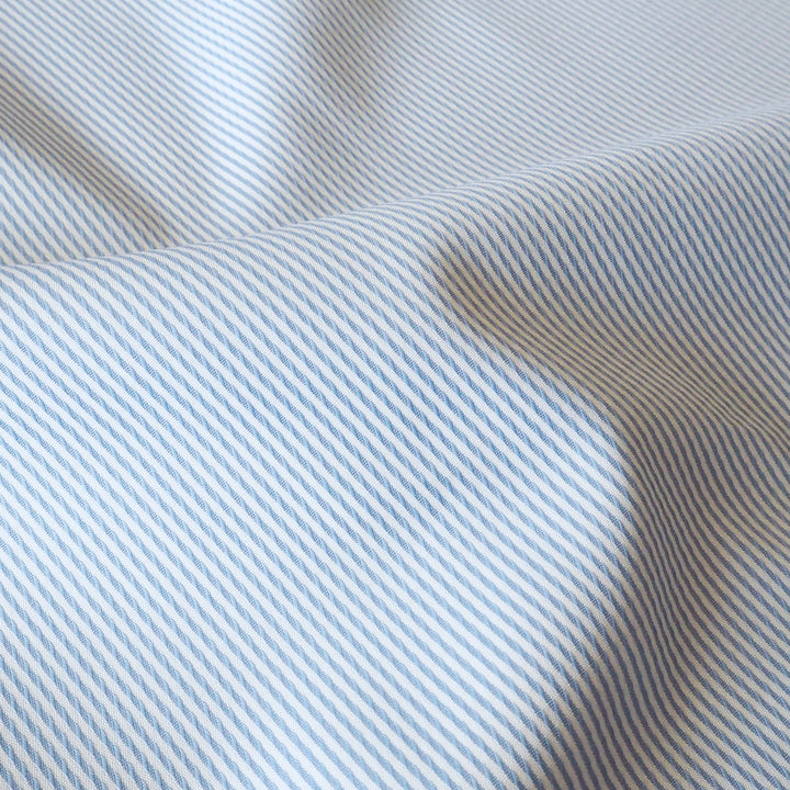 A close-up of draped fabric with a fine diagonal stripe pattern in light blue and off-white.