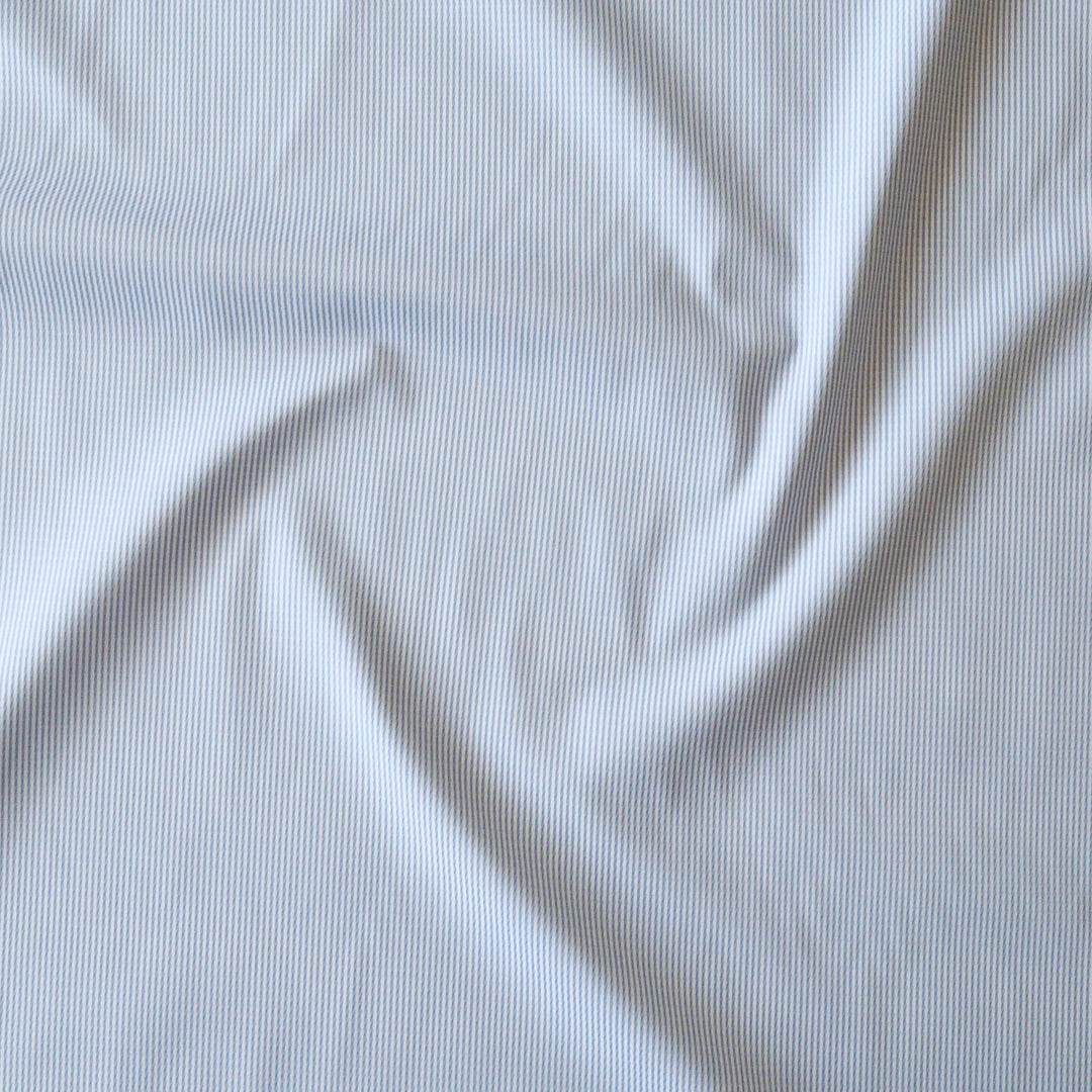 A close-up of white stripe fabric with a soft, swirled drape showing the fine vertical texture.