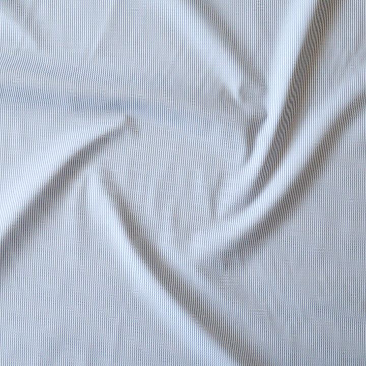 A close-up of white stripe fabric with a soft, swirled drape showing the fine vertical texture.