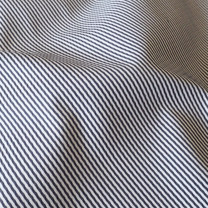 A close-up of a striped fabric with thin navy and white diagonal stripes, showing soft folds and texture.