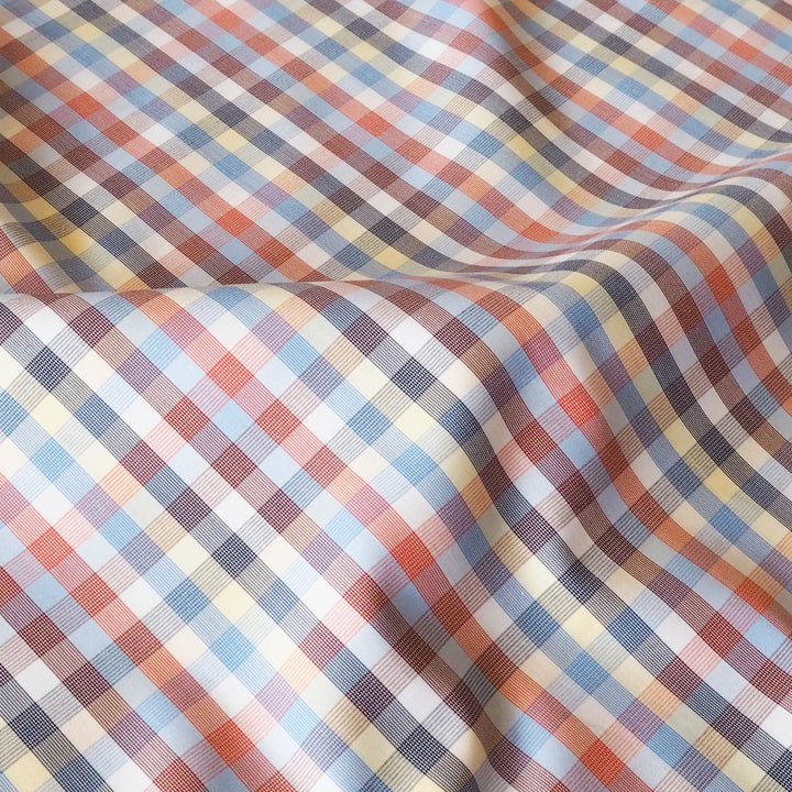 A close-up of a plaid fabric with a multicolor checkered pattern of blue, orange, beige, and dark gray.