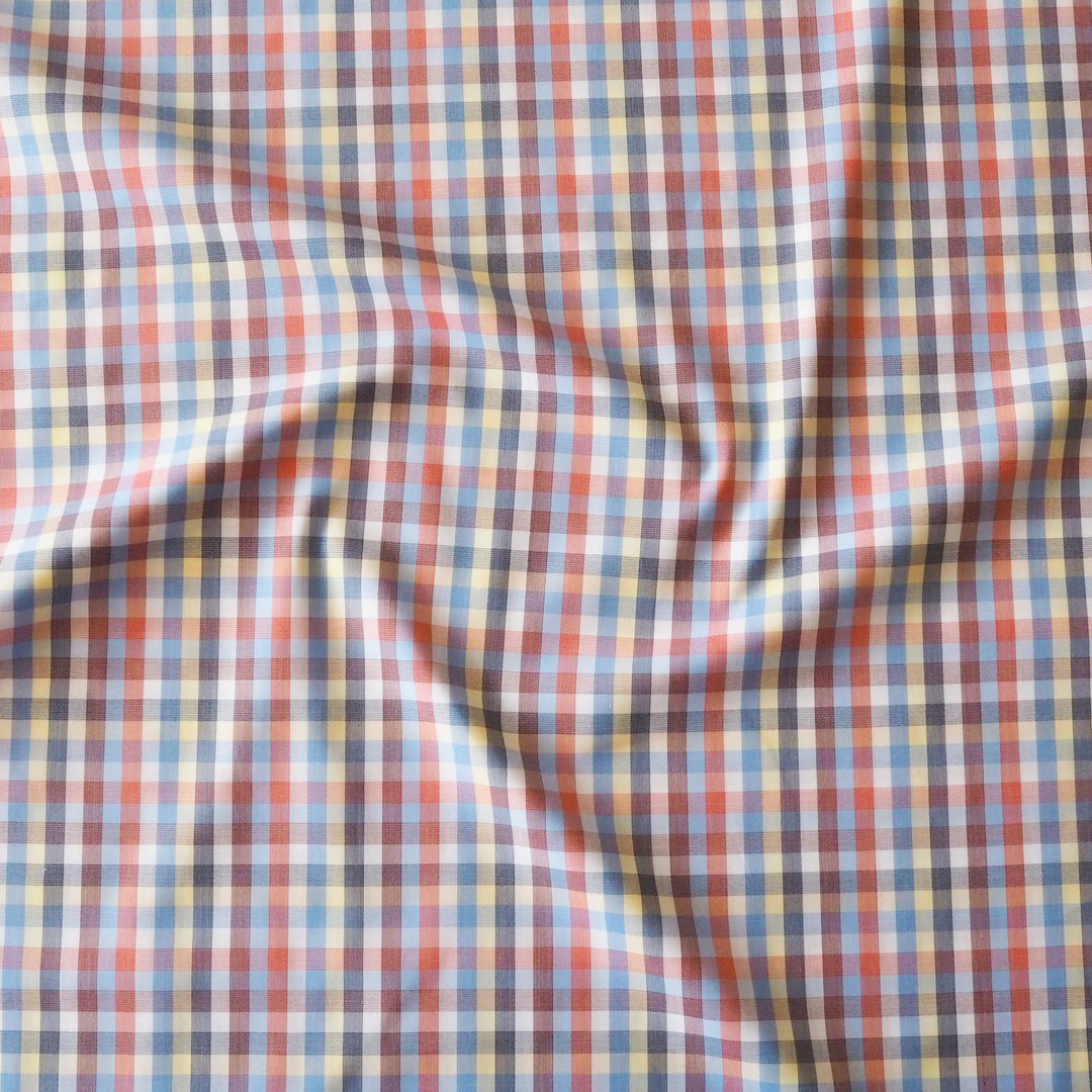 A close-up of draped plaid fabric with a multicolor checkered pattern featuring red, blue, yellow, white, and dark gray lines.