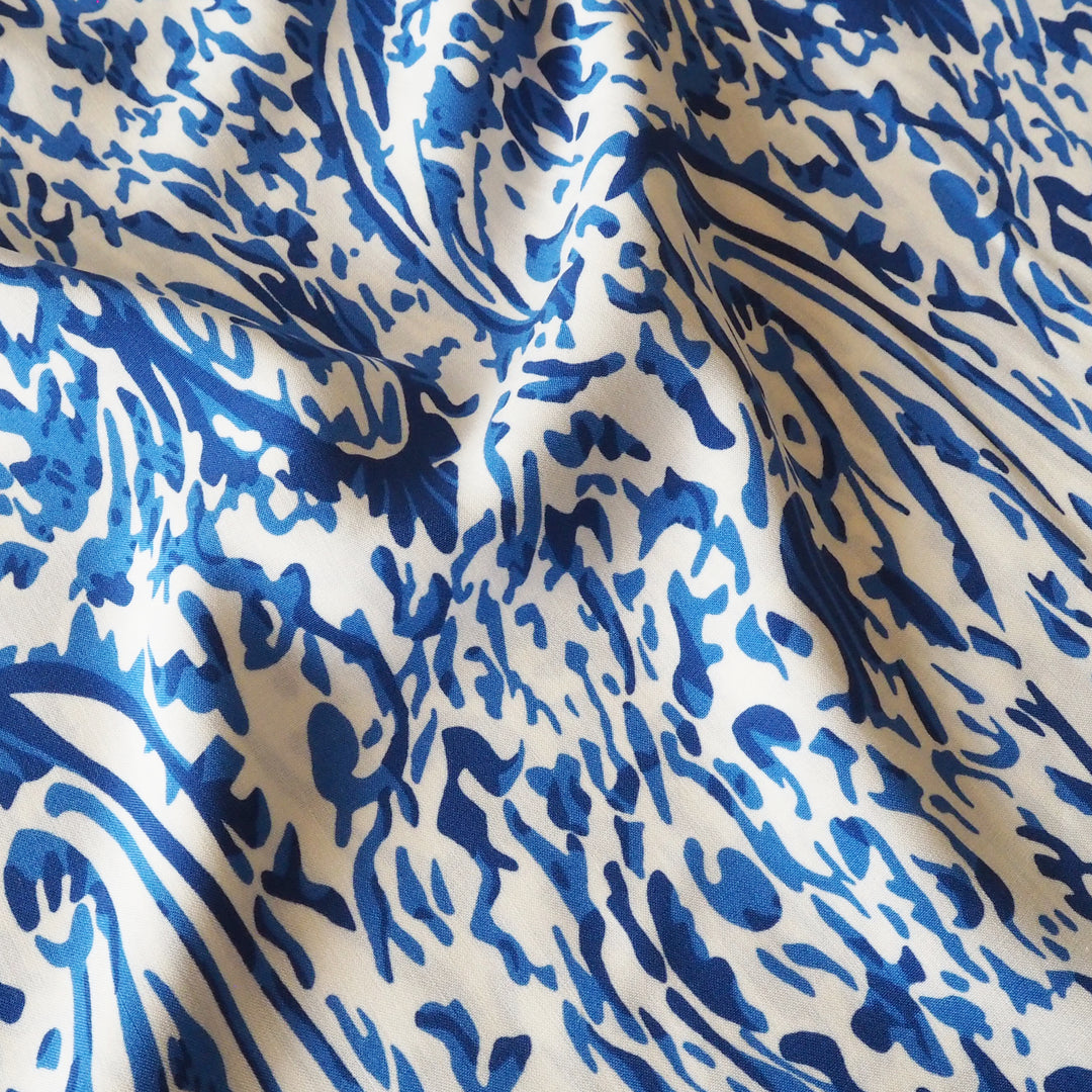 A close-up of draped fabric featuring a bold blue abstract brushstroke pattern on an off white background.