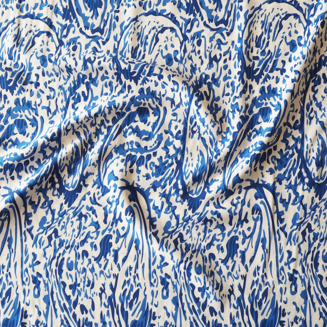 Blue and white abstract patterned fabric with a flowing, marbled design, shown draped with soft folds.