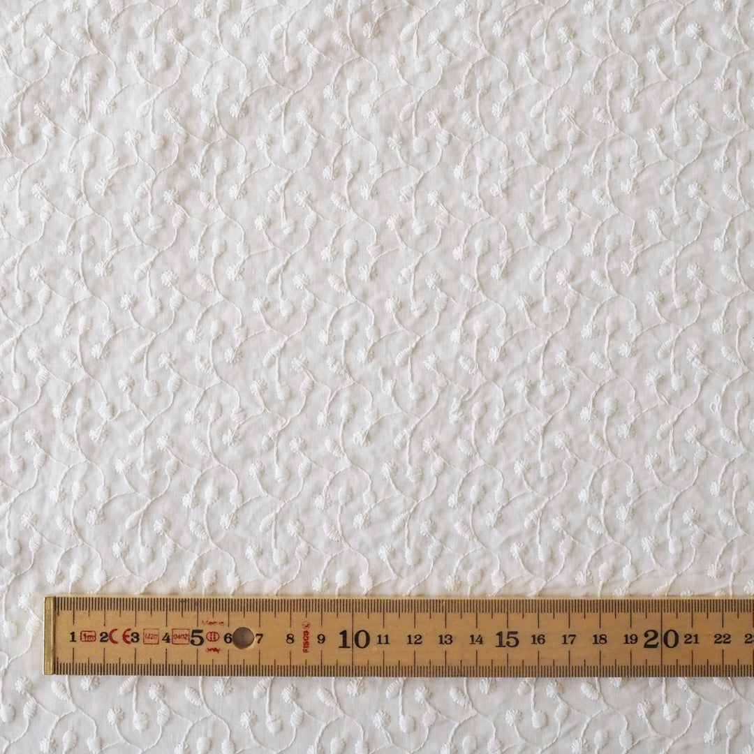 Textured white fabric with a wooden ruler at the bottom for scale.