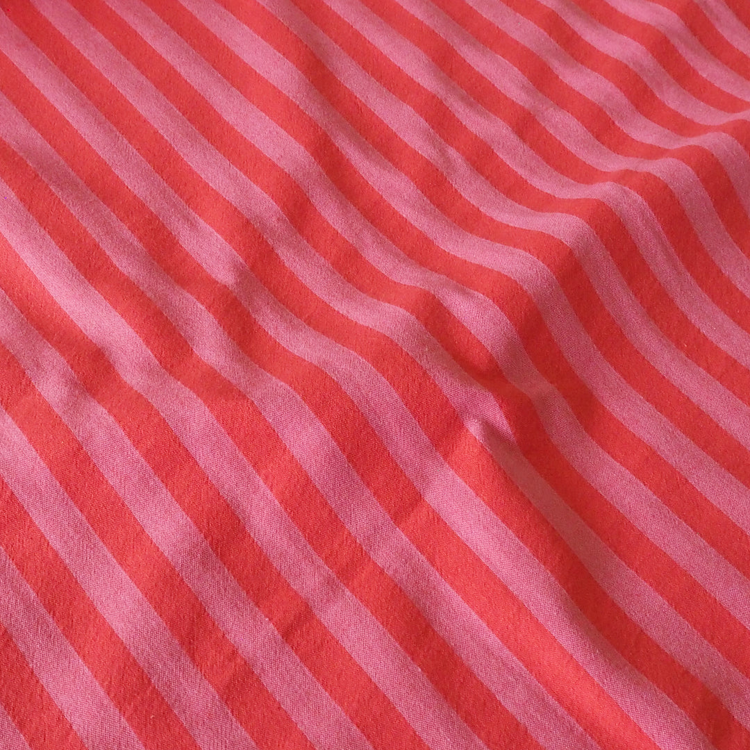 A close-up of a striped fabric with alternating wavy diagonal stripes in coral red and light pink.