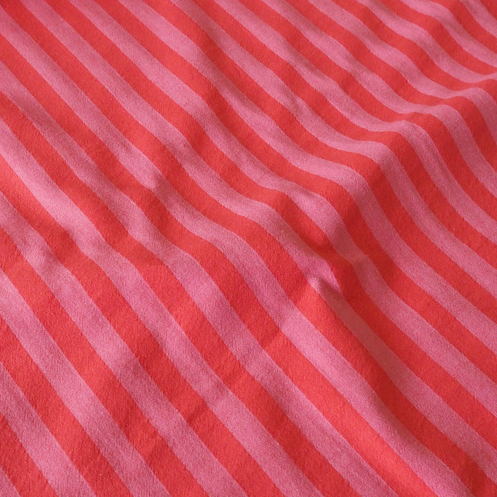 A close-up of a striped fabric with alternating wavy diagonal stripes in coral red and light pink.