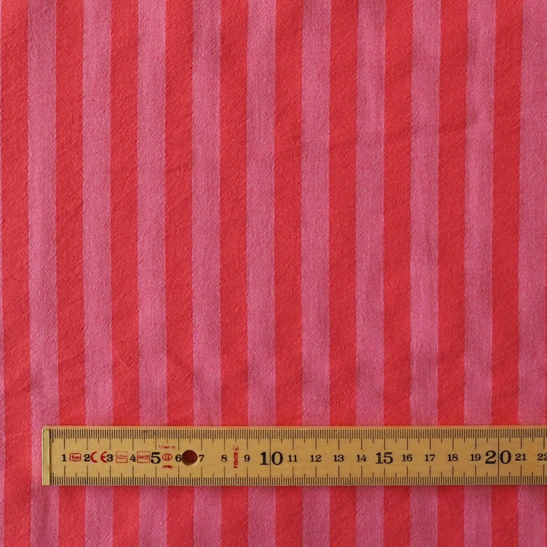 Pink and red vertically striped fabric with a wooden ruler showing measurements at the bottom to indicate scale.