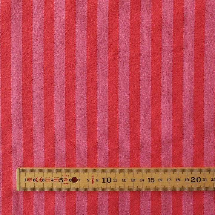 Pink and red vertically striped fabric with a wooden ruler showing measurements at the bottom to indicate scale.
