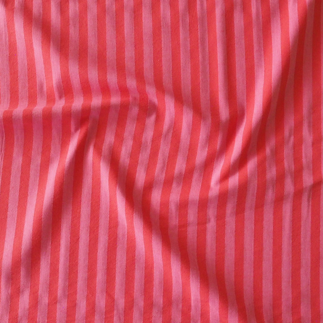 A close-up of a fabric material with vertical stripes in coral red and light pink, showing a soft texture and gentle folds.