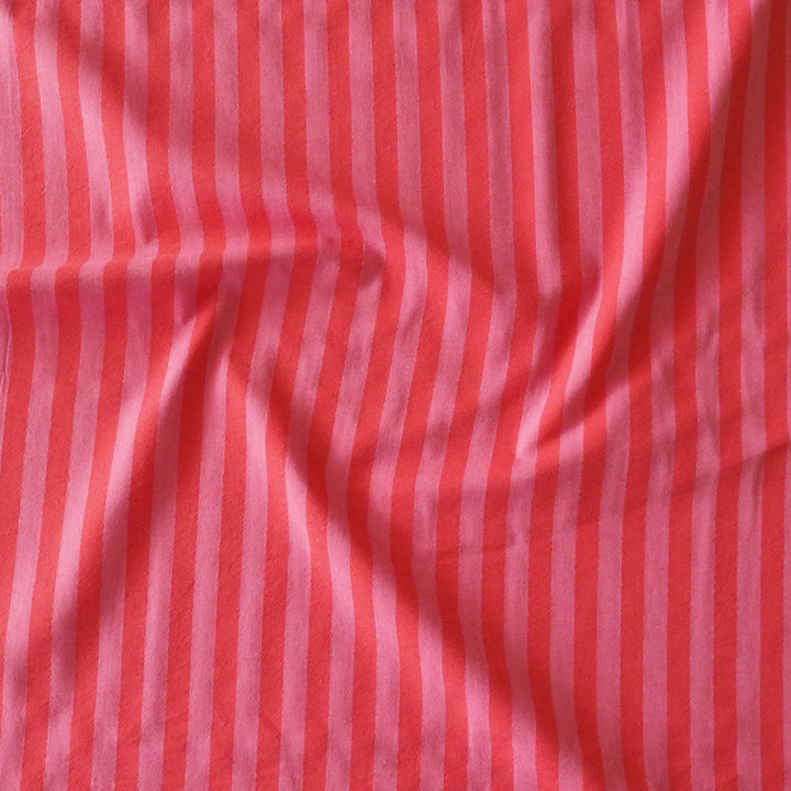 A close-up of a fabric material with vertical stripes in coral red and light pink, showing a soft texture and gentle folds.