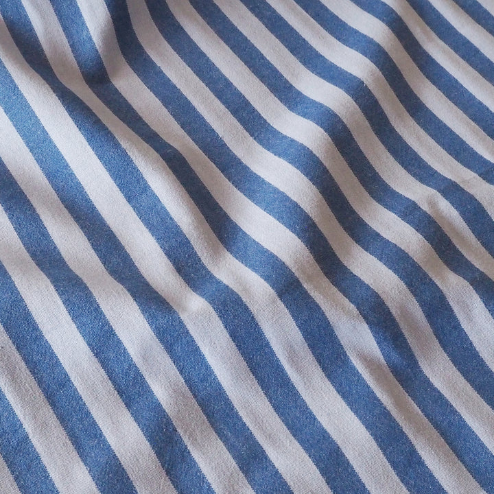 A close-up of a blue striped fabric with a soft, textured weave and gentle folds.