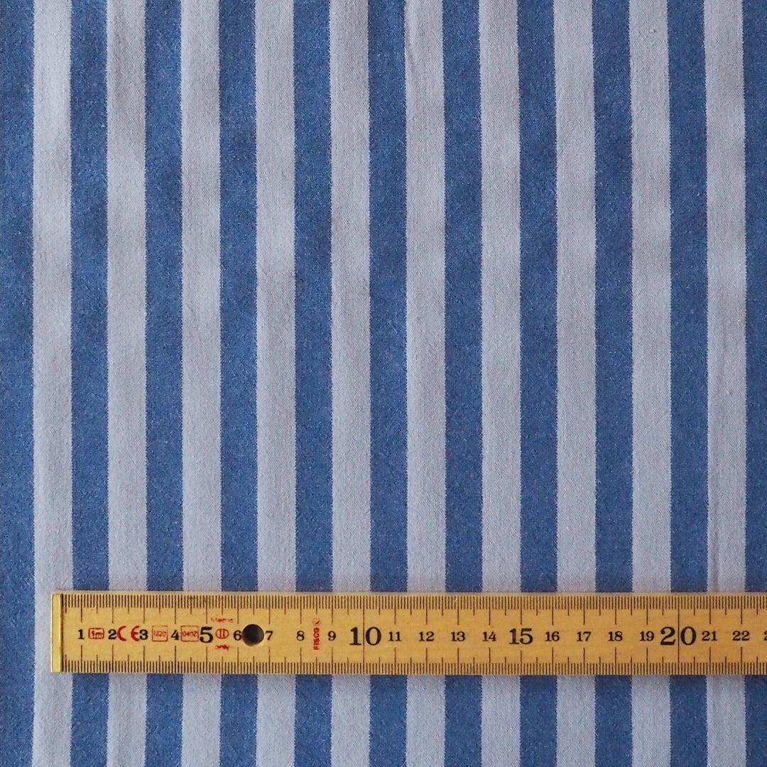 Blue vertically striped fabric with a wooden ruler laid horizontally across the bottom to show scale.