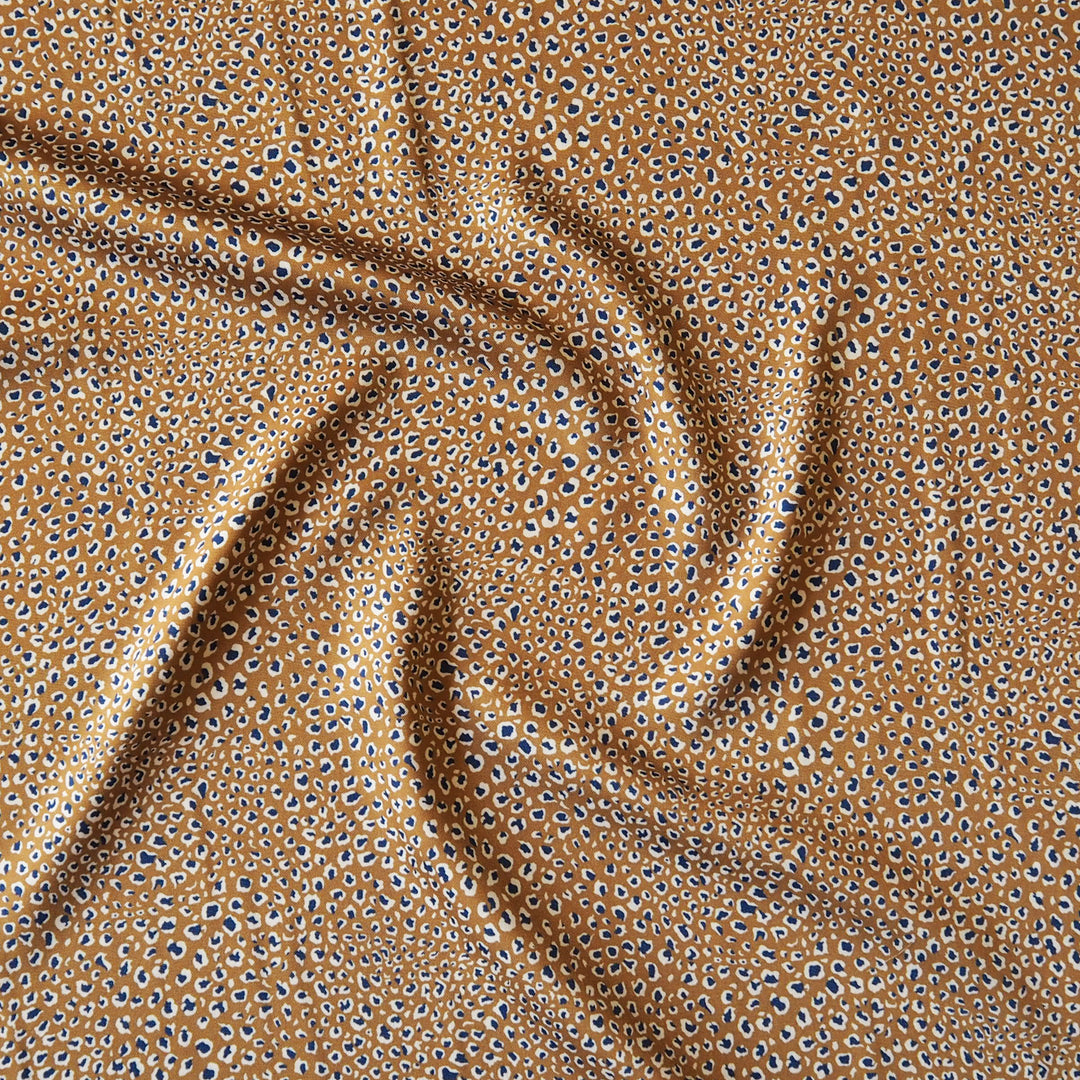 A close-up of draped fabric with a repeating leopard-like spot pattern in tan, brown, black, and white.