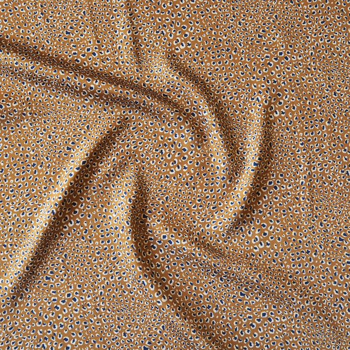 A close-up of draped fabric with a repeating leopard-like spot pattern in tan, brown, black, and white.
