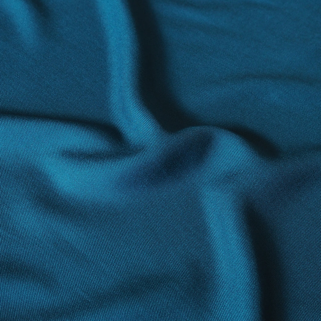 A close-up of draped teal blue fabric with soft folds and a fine knit texture.