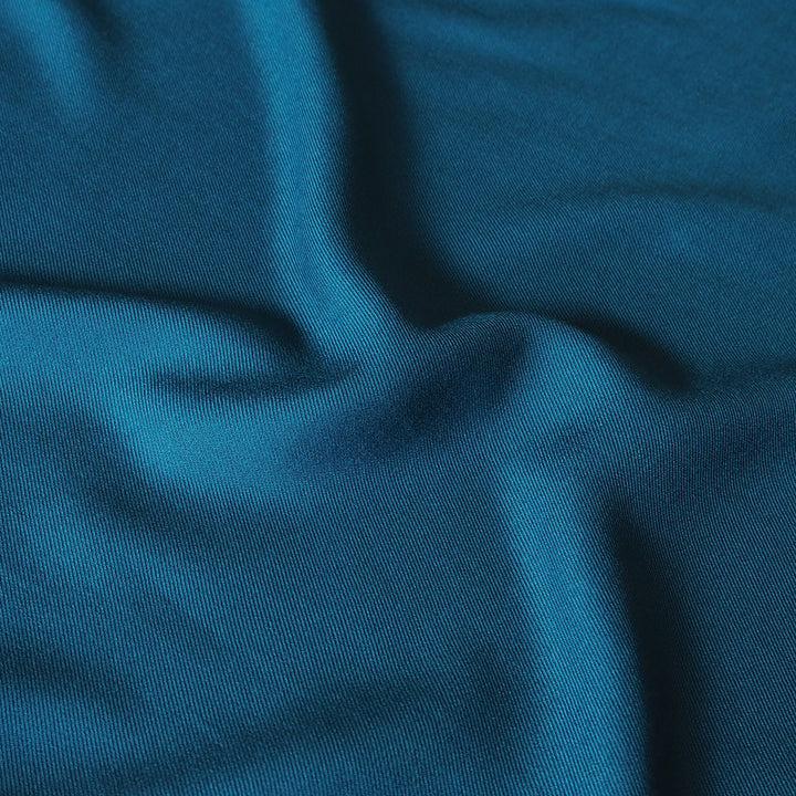 A close-up of draped teal blue fabric with soft folds and a fine knit texture.