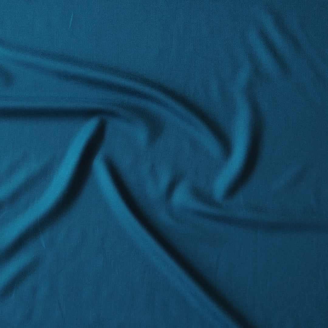 A close-up of draped teal blue fabric with soft folds and a smooth texture.
