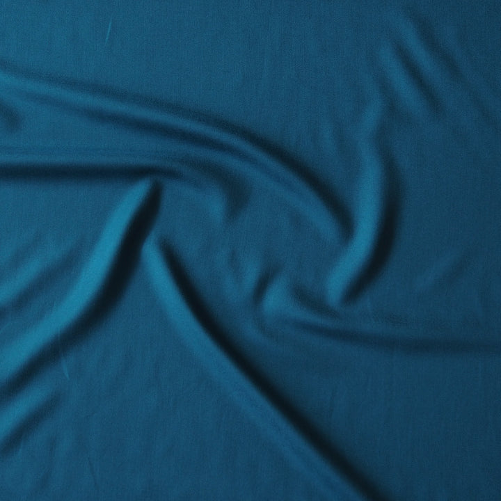 A close-up of draped teal blue fabric with soft folds and a smooth texture.