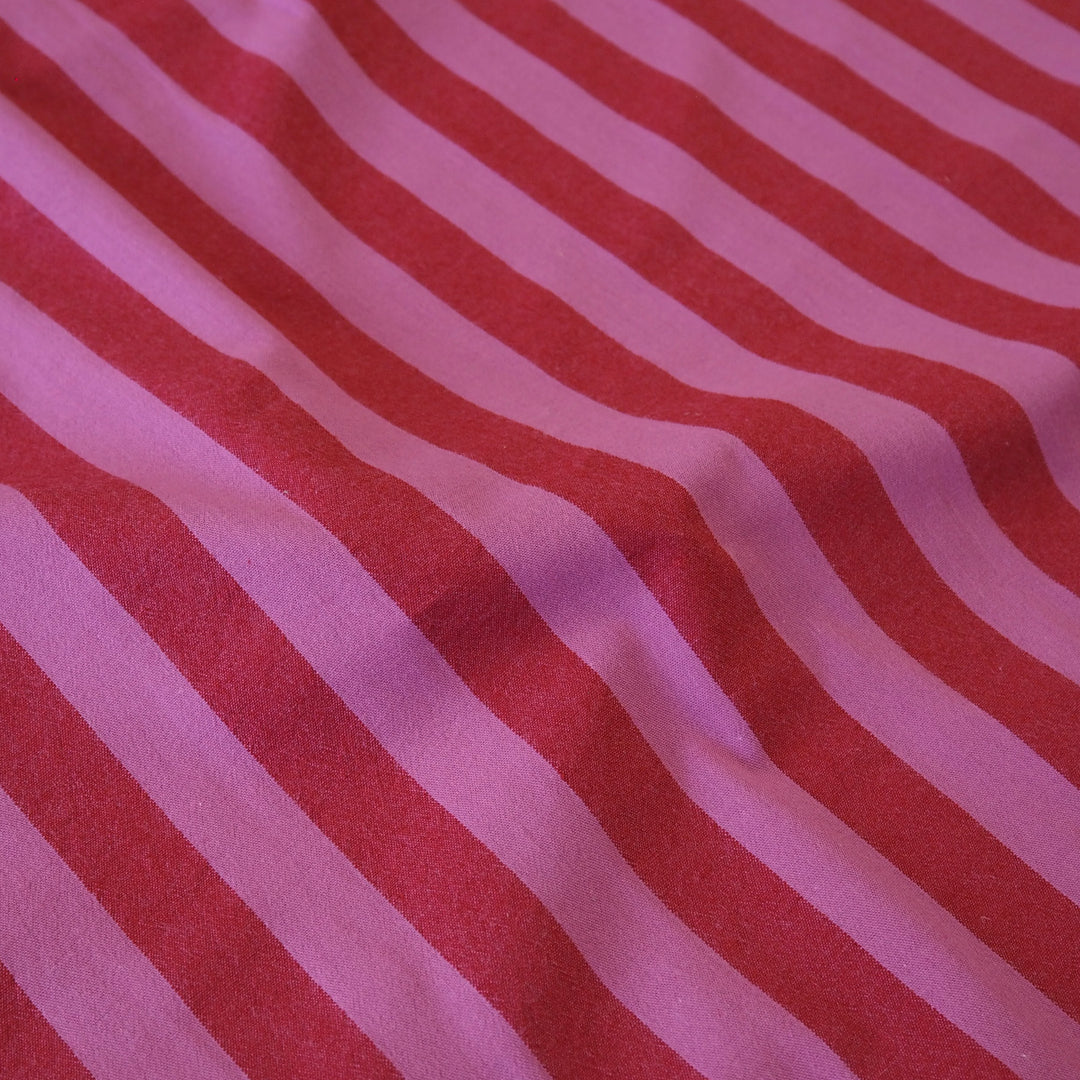 A close-up of a striped fabric with alternating diagonal bands of red and light pink, showing a soft textured weave with gentle folds.