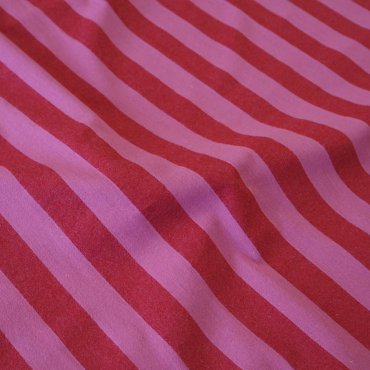 A close-up of a striped fabric with alternating diagonal bands of red and light pink, showing a soft textured weave with gentle folds.